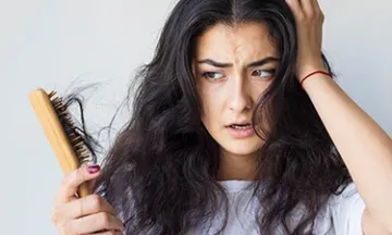 Woman distressed over hair loss, holding a brush with shed hair.